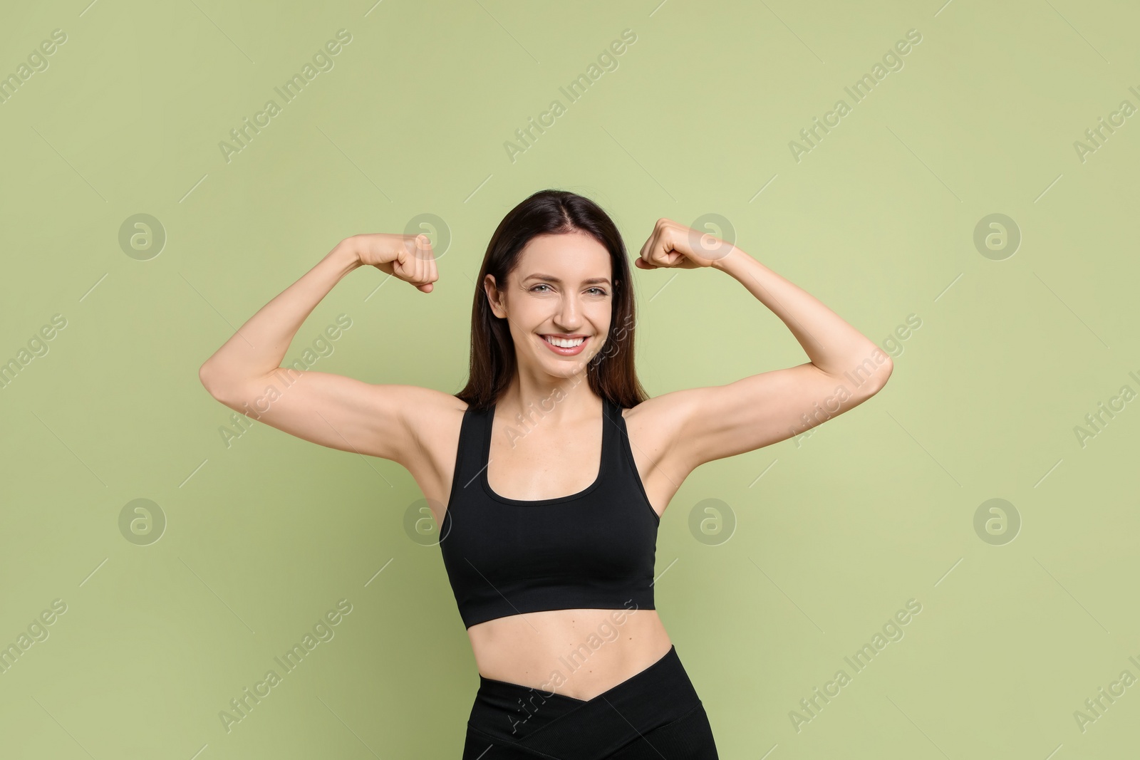 Photo of Happy young woman with slim body showing her muscles on green background