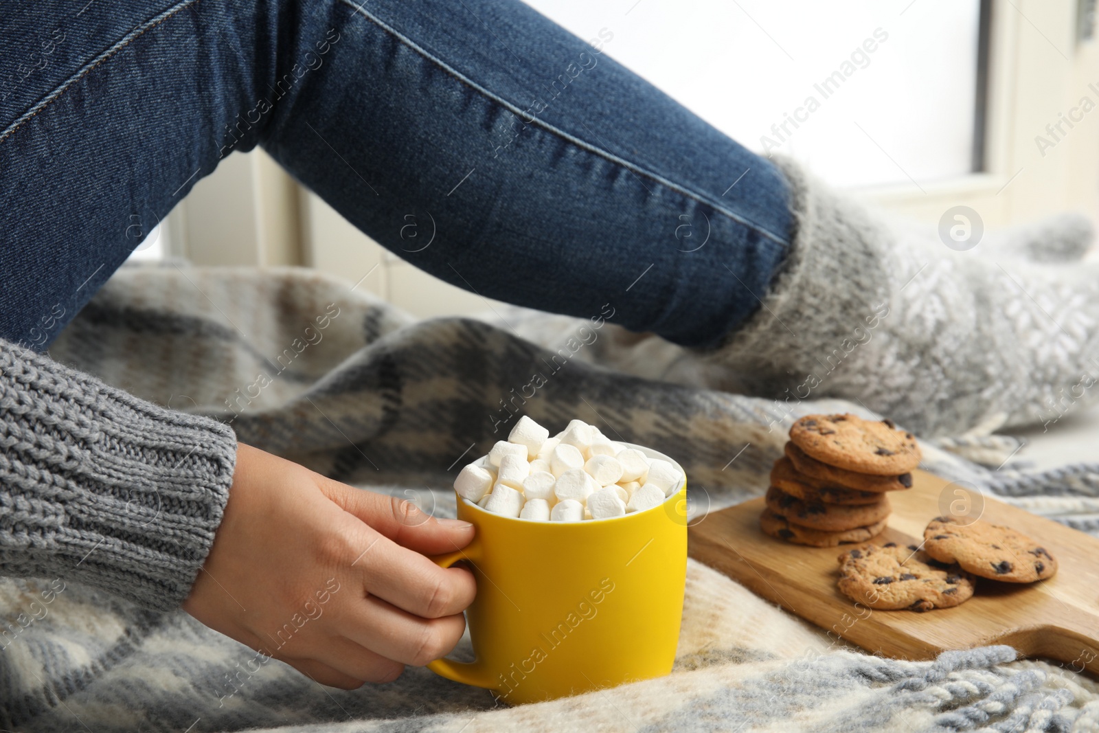 Photo of Woman with cup of hot cocoa sitting on window sill, closeup. Winter drink