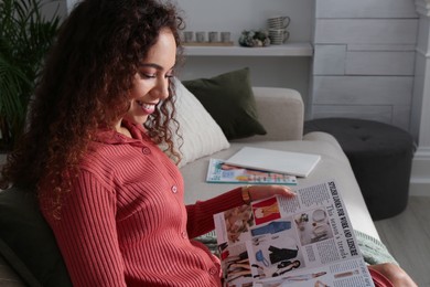 Photo of Young African-American woman reading fashion magazine at home