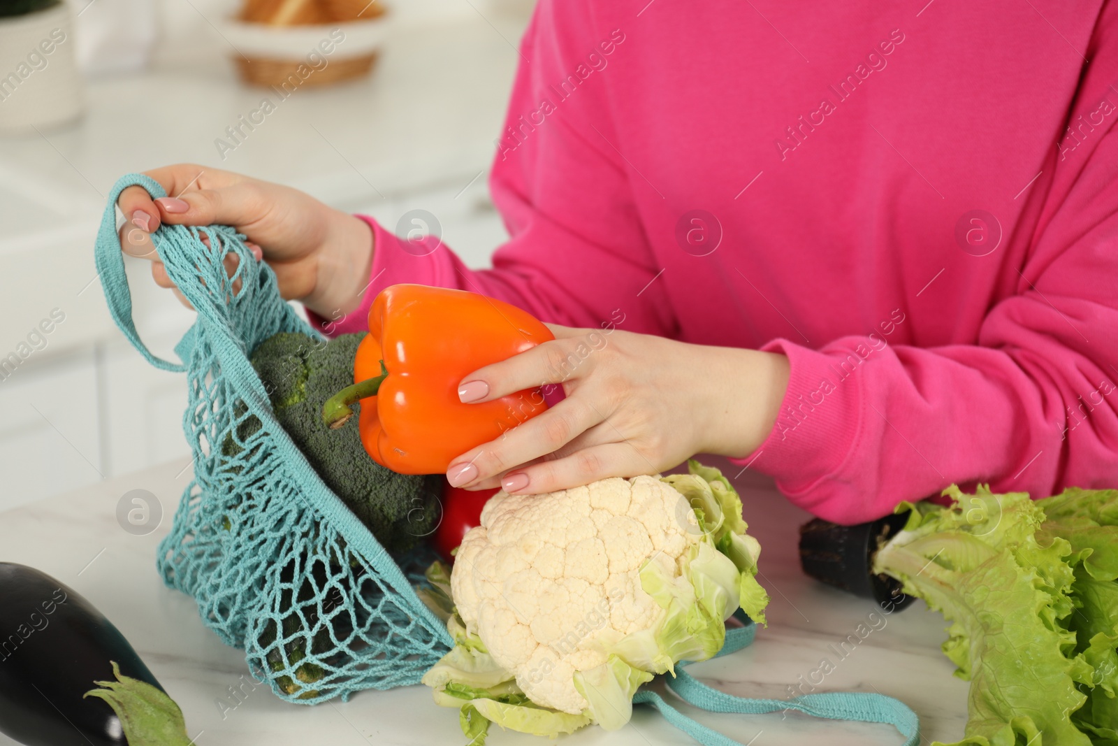 Photo of Woman taking pepper out from string bag at light marble table, closeup