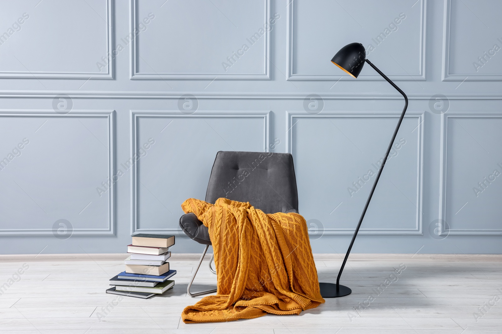 Photo of Comfortable armchair with blanket, books and lamp near grey wall indoors
