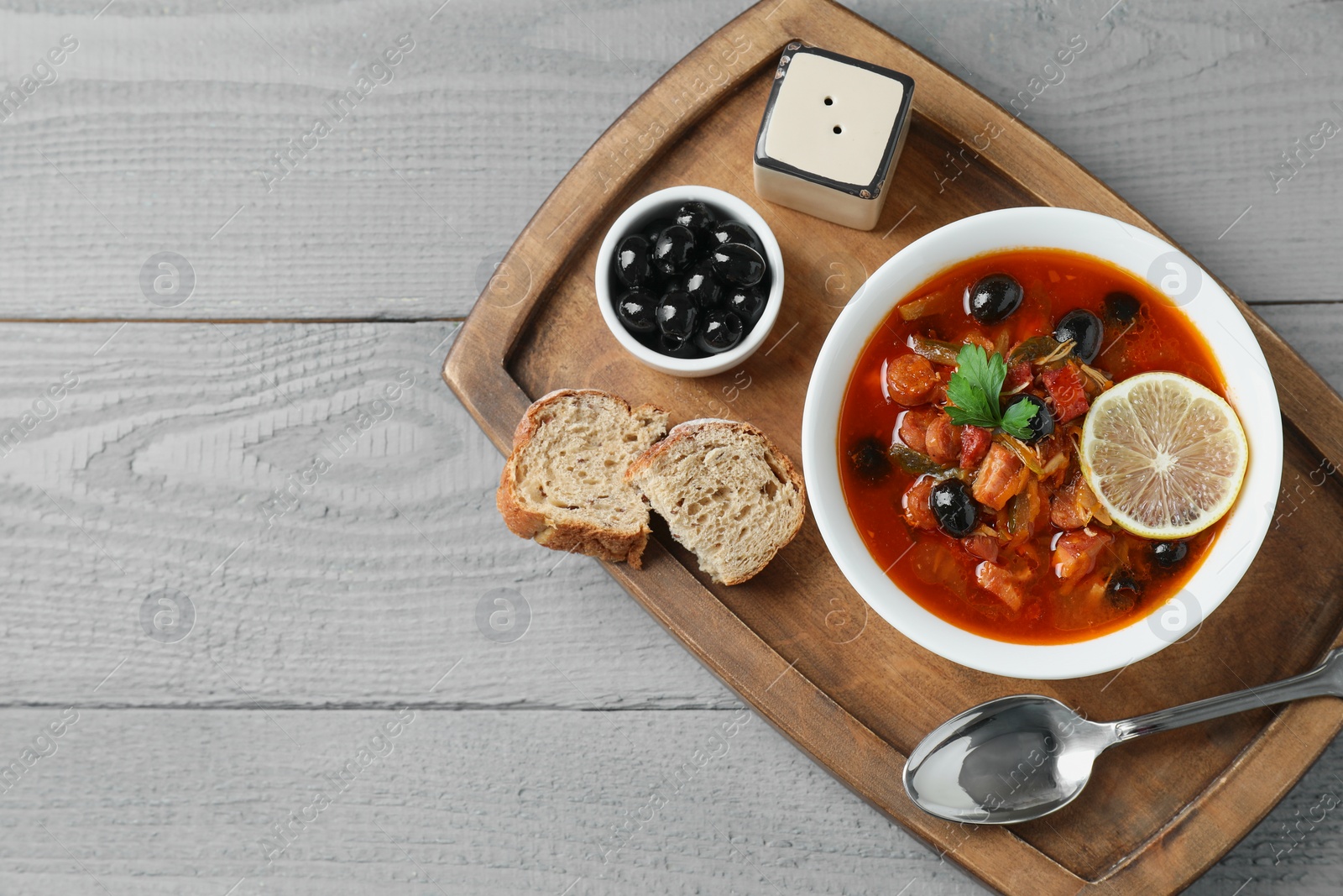 Photo of Meat solyanka soup with sausages, olives and vegetables in bowl served on grey wooden table, top view. Space for text