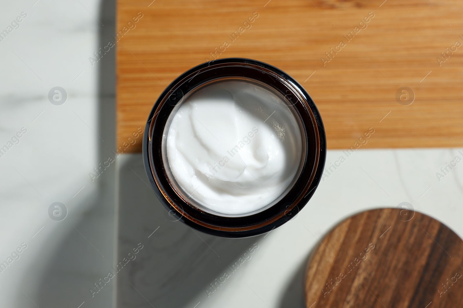 Photo of Board with open jar of cosmetic cream on white table, top view