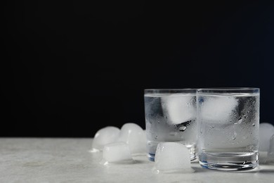 Photo of Shot glasses of vodka with ice on light grey table against black background. Space for text