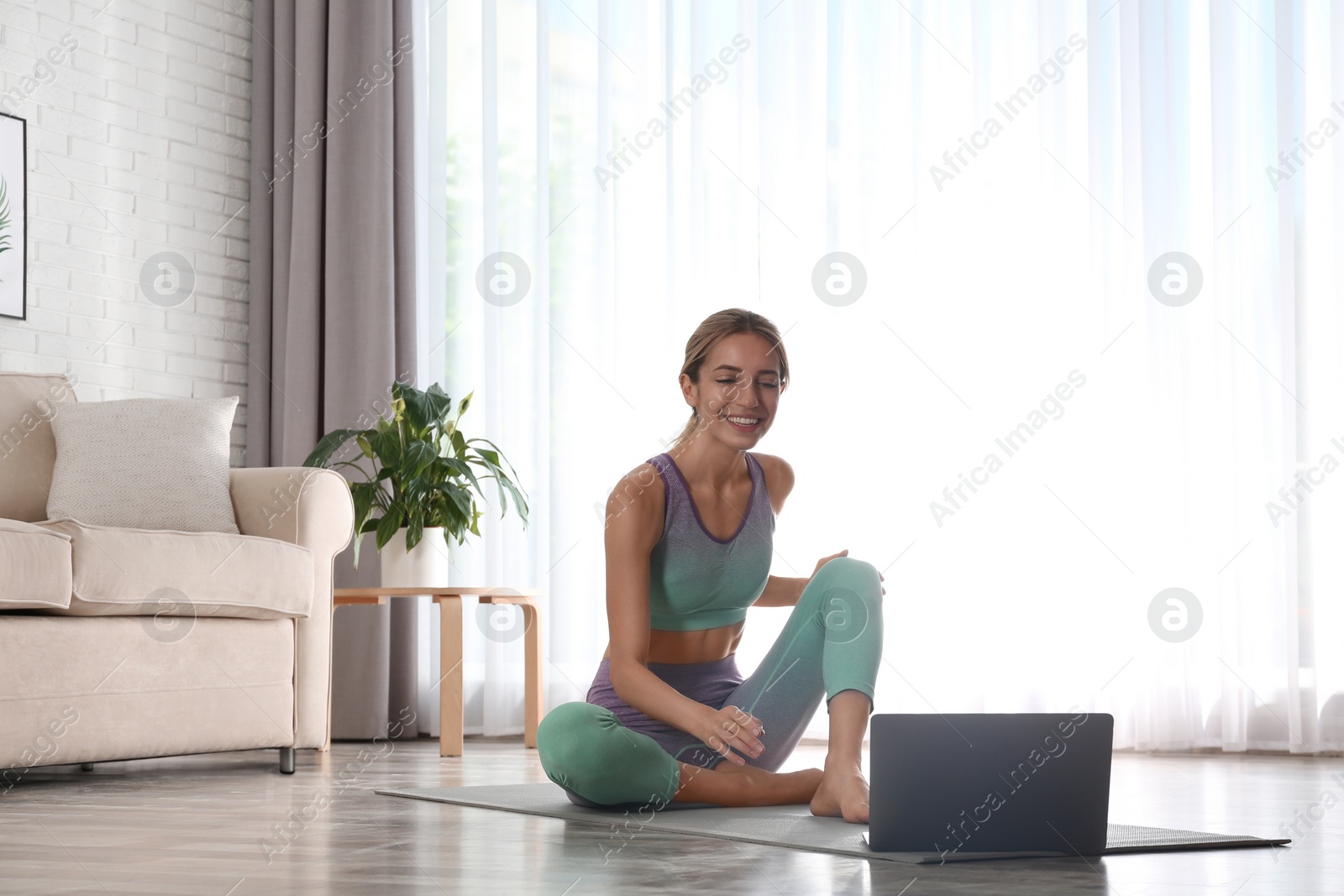 Photo of Woman having online video class via laptop at home. Distance yoga course during coronavirus pandemic