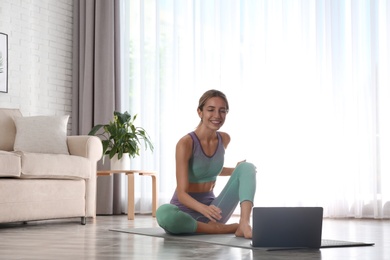 Photo of Woman having online video class via laptop at home. Distance yoga course during coronavirus pandemic