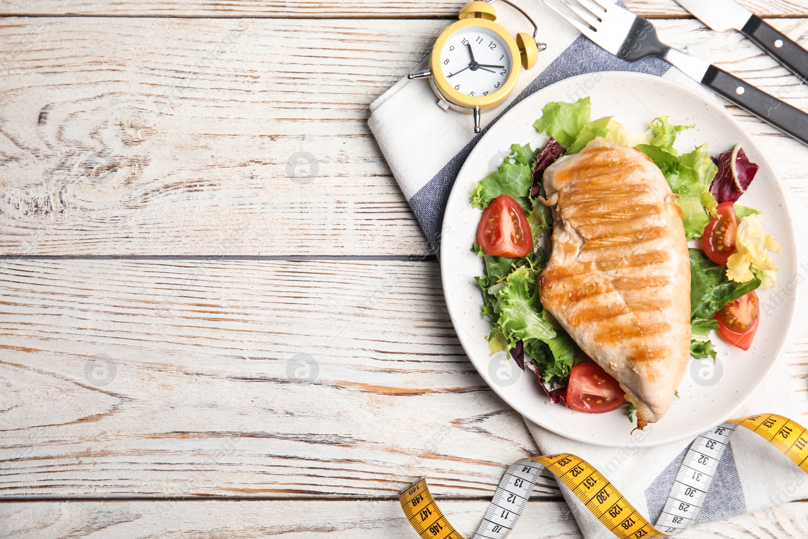 Photo of Plate of appetizing food, alarm clock and measuring tape on white wooden table, flat lay with space for text. Nutrition regime