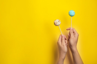 Photo of Woman holding bright delicious cake pops on color background, closeup. Space for text