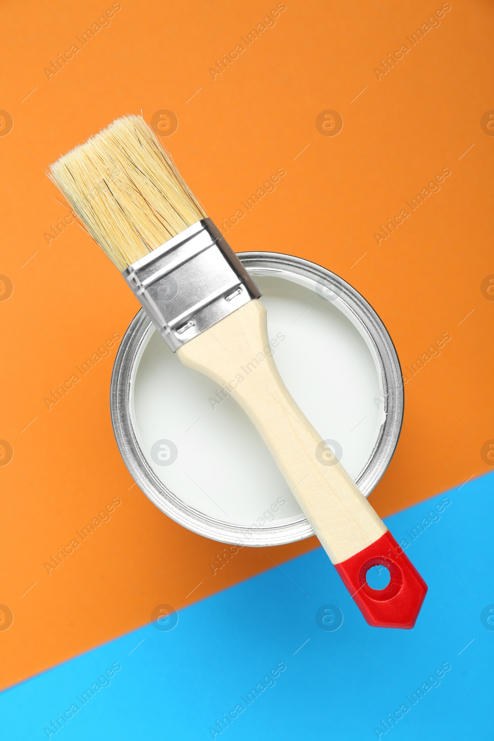 Photo of Can of white paint with brush on color background, top view