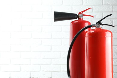 Photo of Fire extinguishers against white brick wall, closeup. Space for text