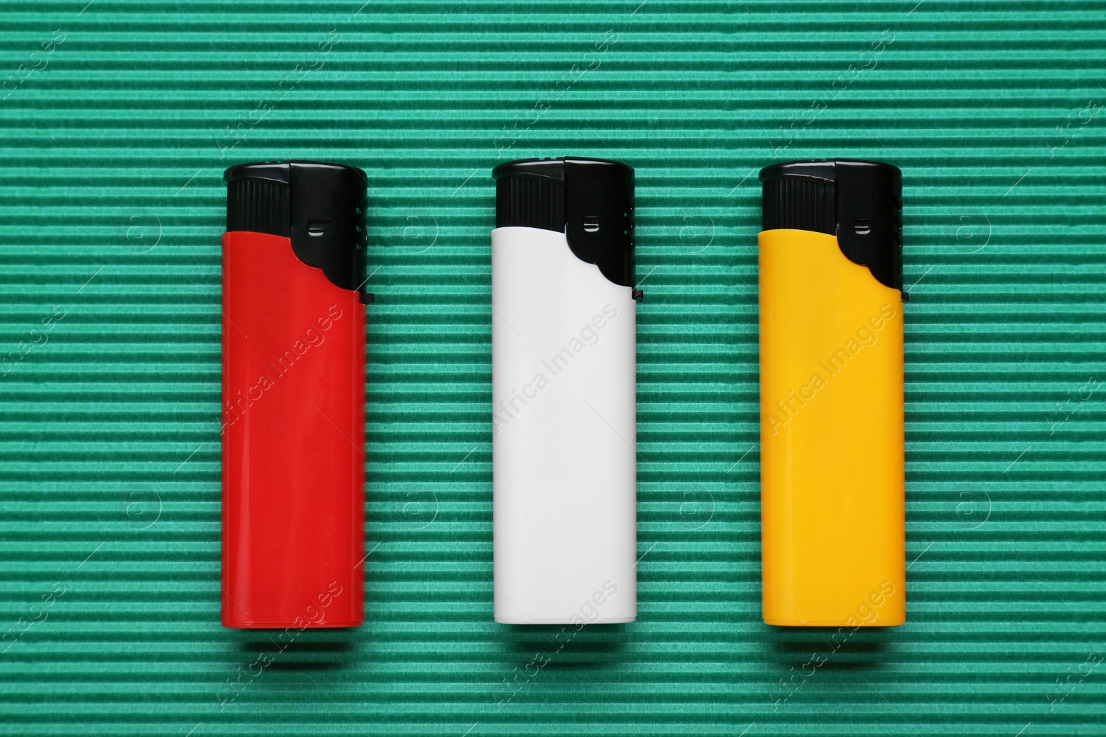 Photo of Stylish small pocket lighters on green corrugated fiberboard, flat lay