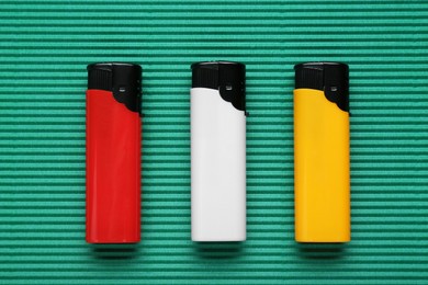 Stylish small pocket lighters on green corrugated fiberboard, flat lay