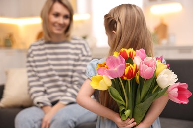 Photo of Little girl hiding bouquet of tulips for mom at home, selective focus. Happy Mother's Day