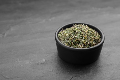 Photo of Bowl with dried thyme on black table, closeup. Space for text