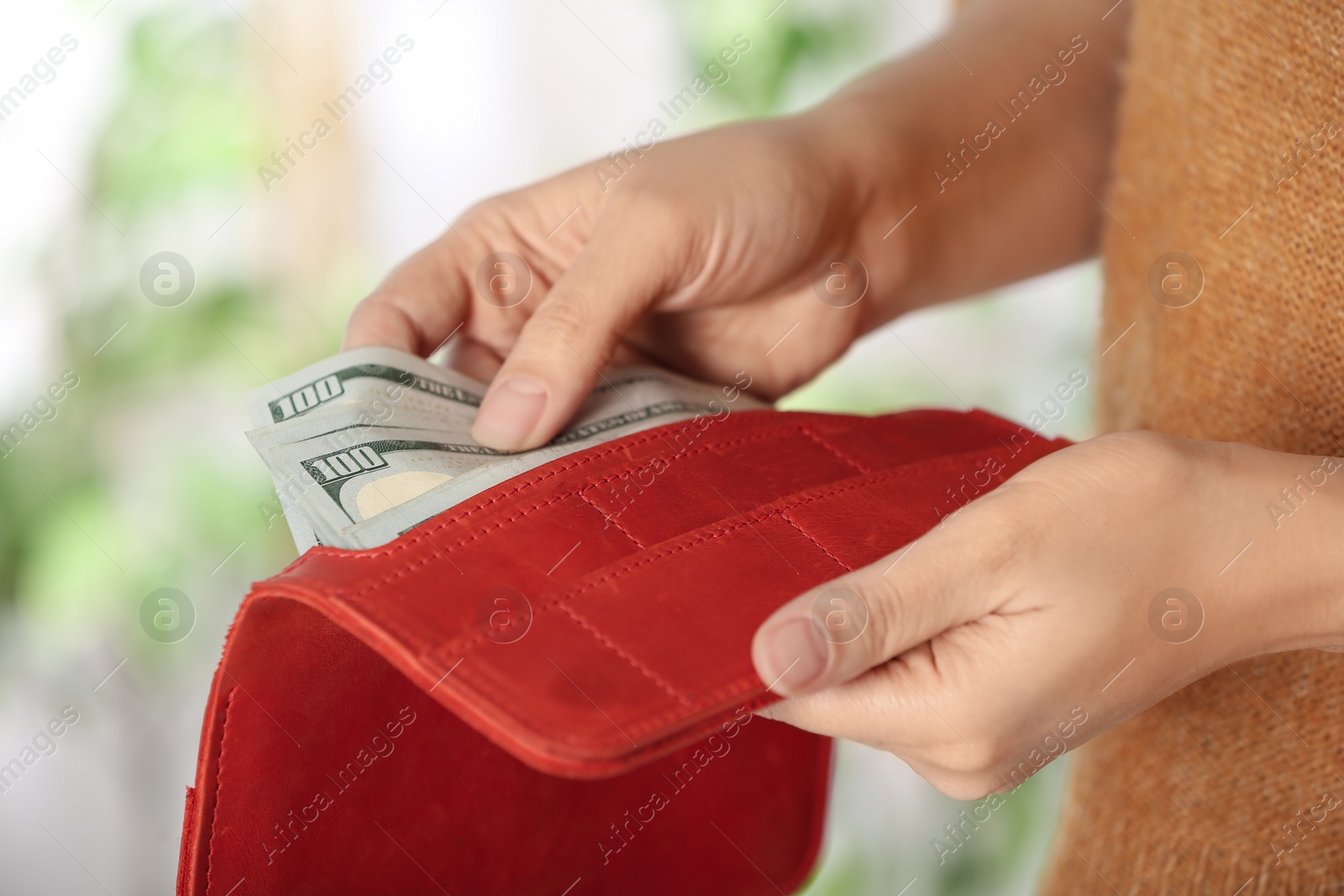 Photo of Woman putting money into wallet on blurred background, closeup