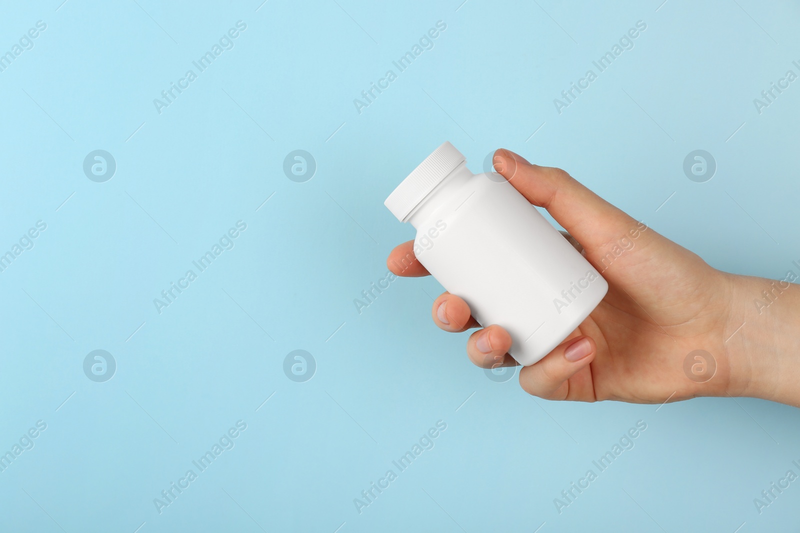 Photo of Woman holding blank white jar of vitamins on light blue background, closeup. Space for text