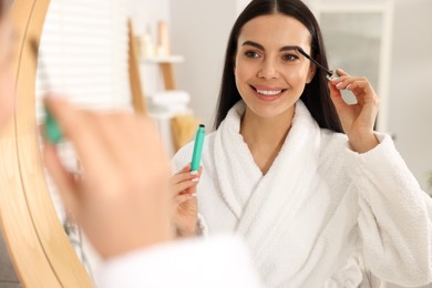 Photo of Beautiful young woman applying mascara near mirror in bathroom