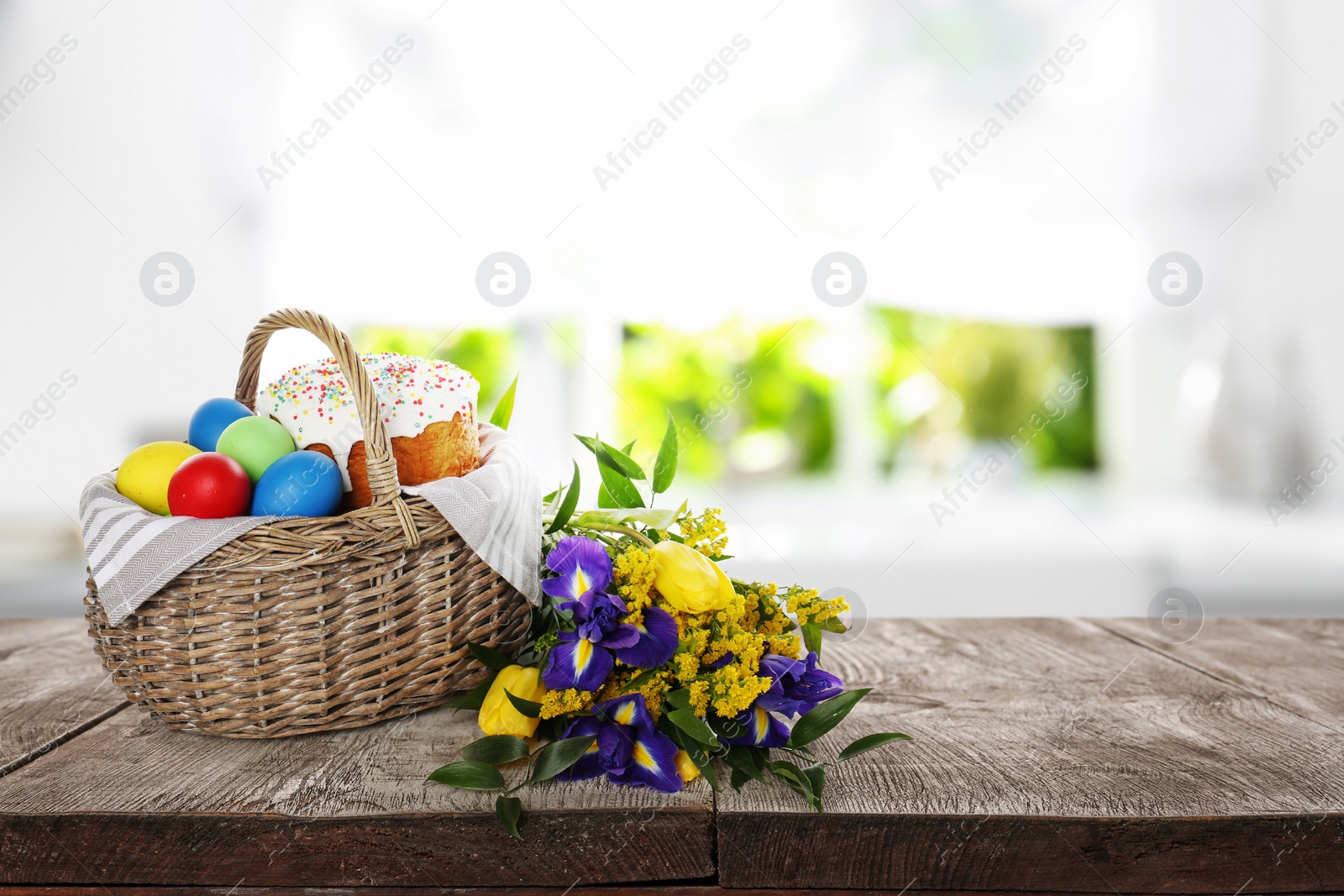 Image of Basket with traditional Easter cake, dyed eggs and flowers on wooden table indoors. Space for text