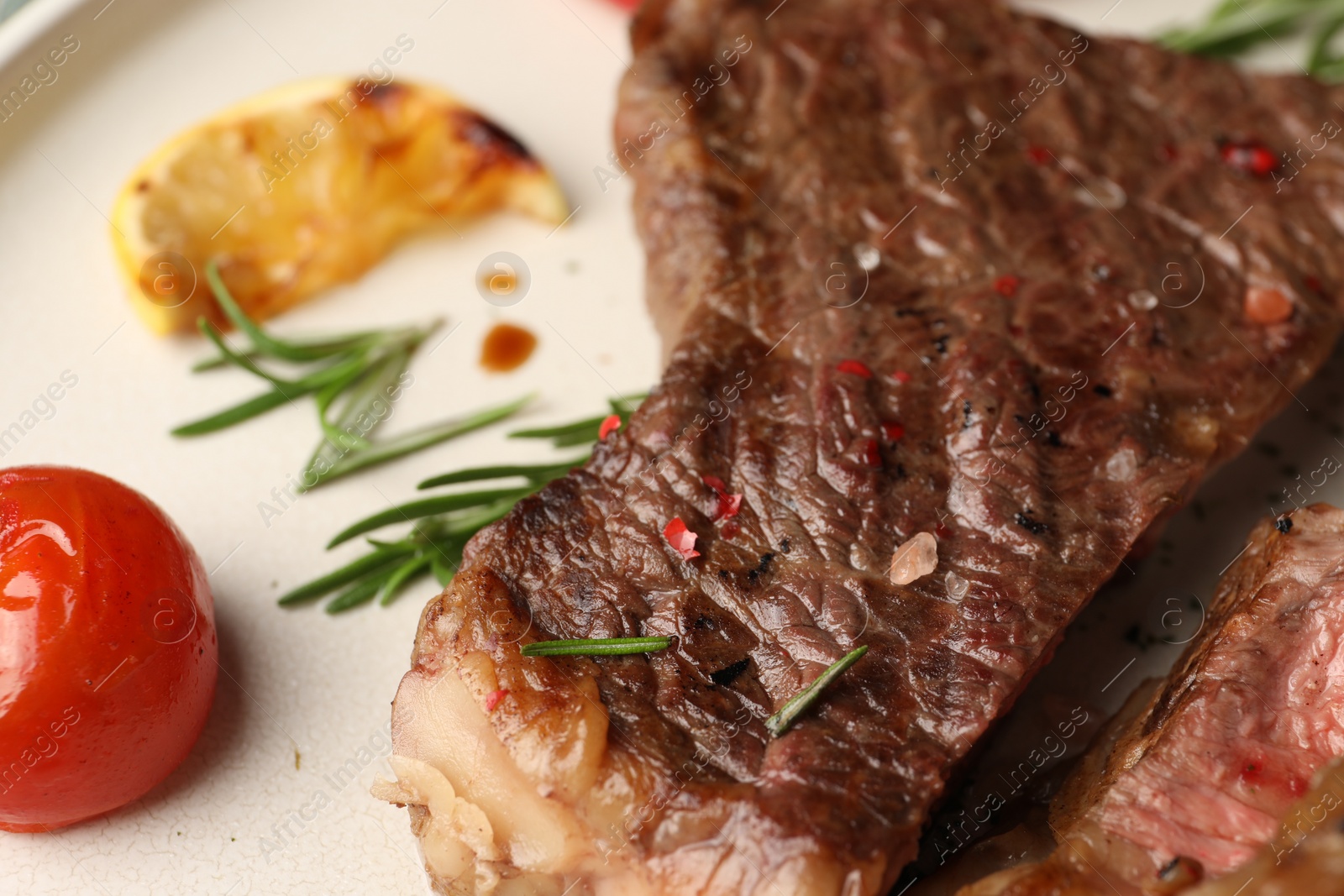 Photo of Delicious grilled beef steak, tomato, rosemary and lemon slice on plate, closeup