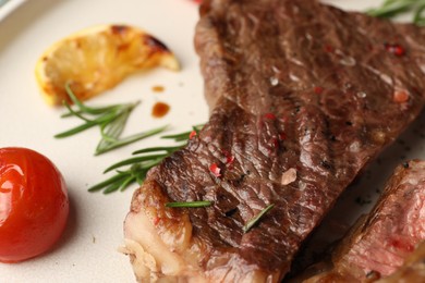 Photo of Delicious grilled beef steak, tomato, rosemary and lemon slice on plate, closeup