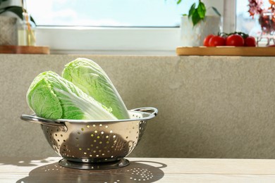 Photo of Fresh Chinese cabbages in colander on light wooden table indoors. Space for text