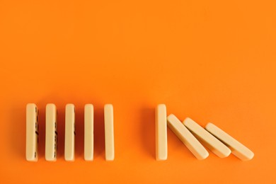 Photo of White domino tiles on orange background, flat lay