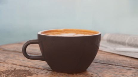 Photo of Cup of delicious coffee and newspaper on wooden table, closeup