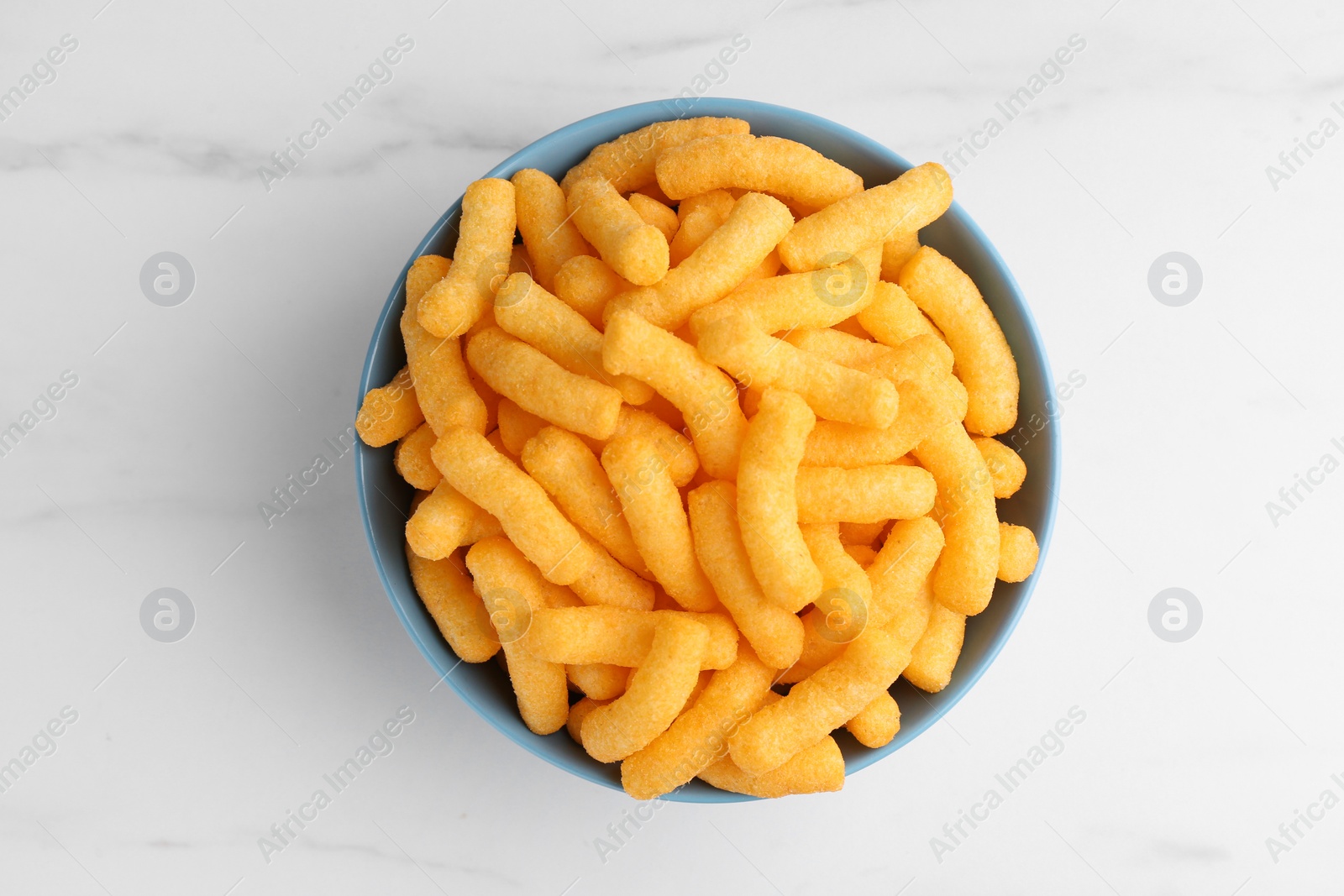 Photo of Bowl of tasty cheesy corn puffs on white marble table, top view