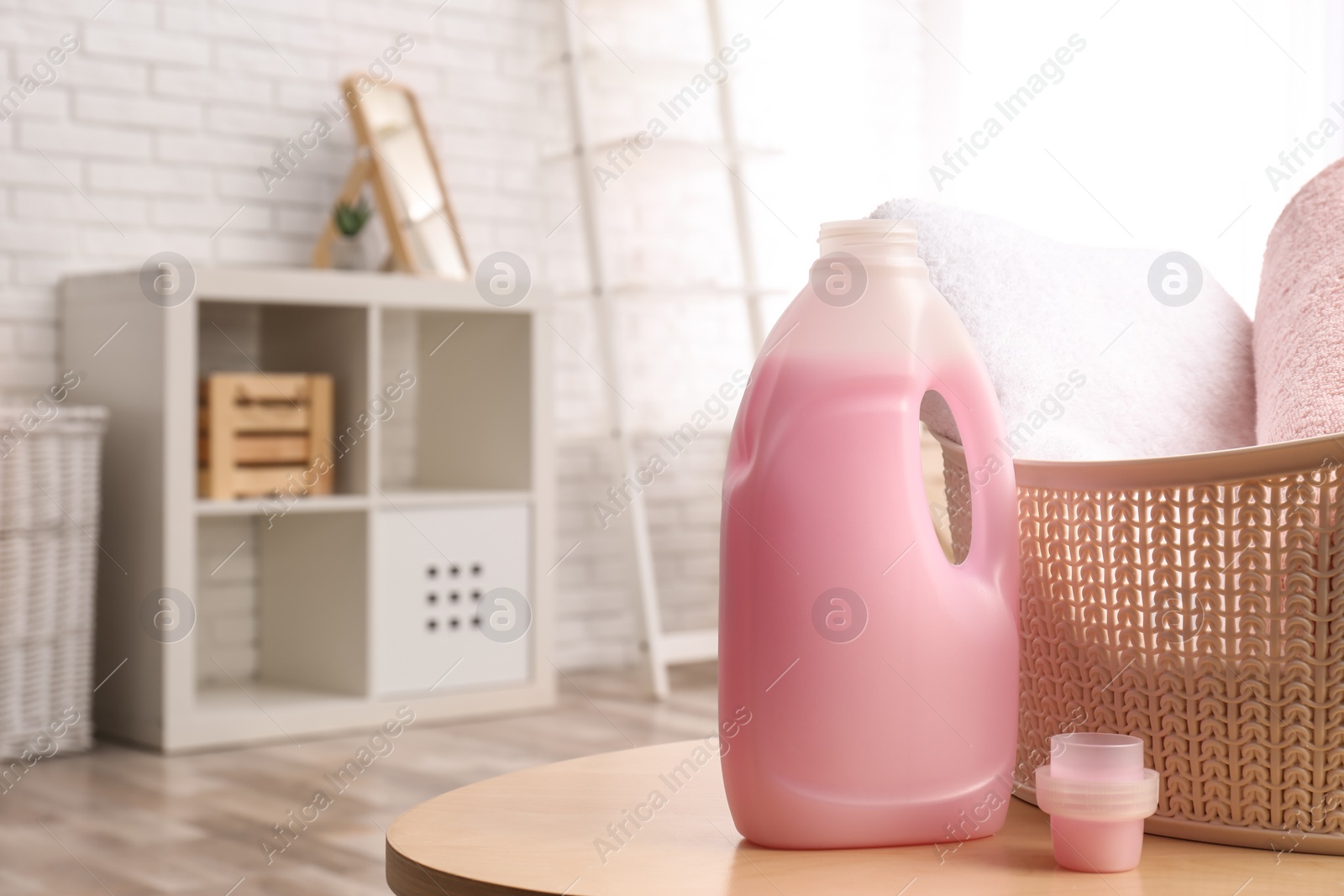 Photo of Bottle of detergent and clean towels on table indoors, space for text. Laundry day