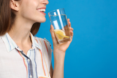 Photo of Young woman drinking lemon water on light blue background, closeup