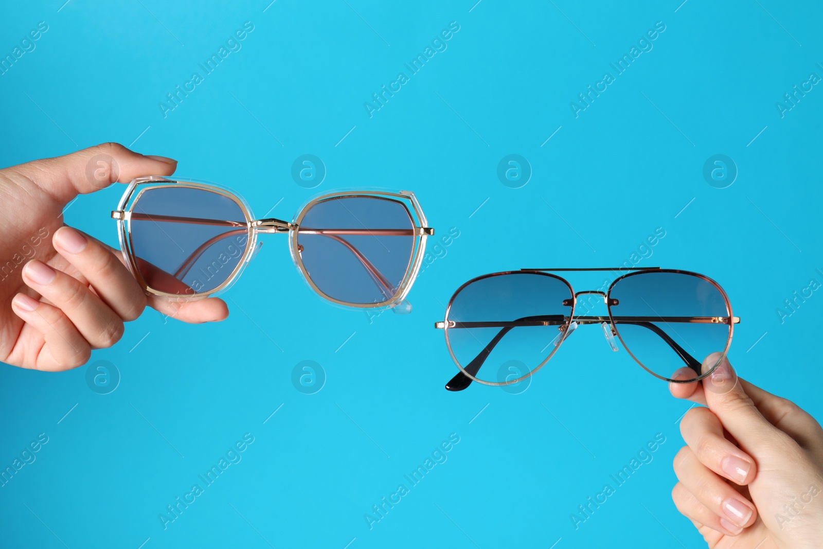 Photo of Women holding stylish sunglasses on light blue background, closeup