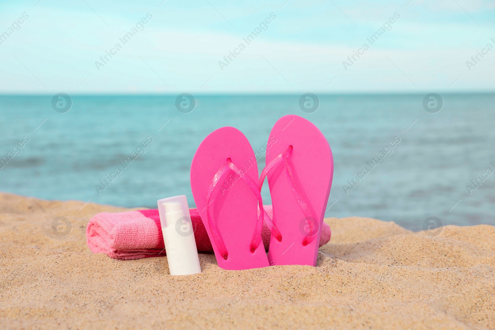 Photo of Beach towel, slippers and sunscreen on sand near sea