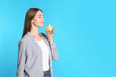 Young woman with glass of lemon water on light blue background. Space for text