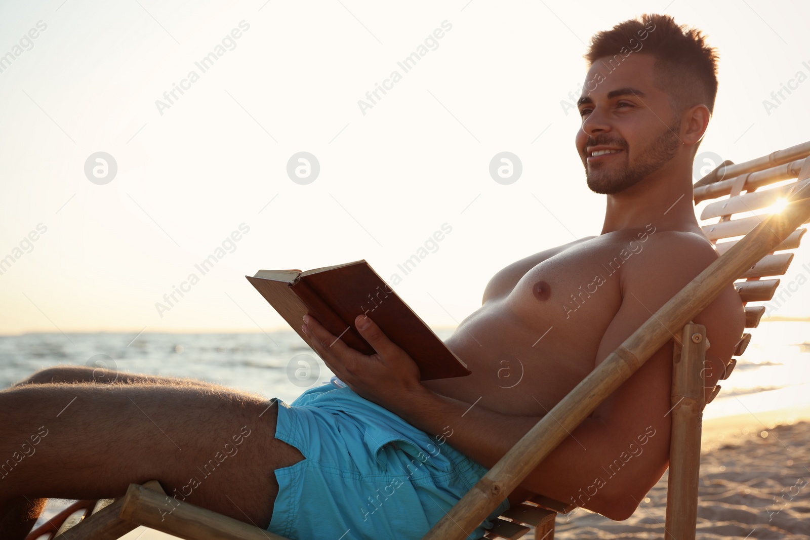 Photo of Young man reading book in deck chair on beach