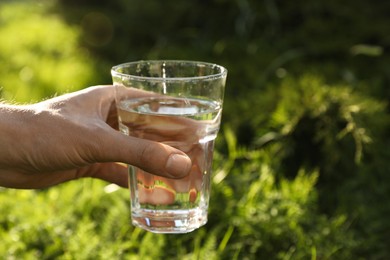 Photo of Man holding glass of fresh water outdoors, closeup