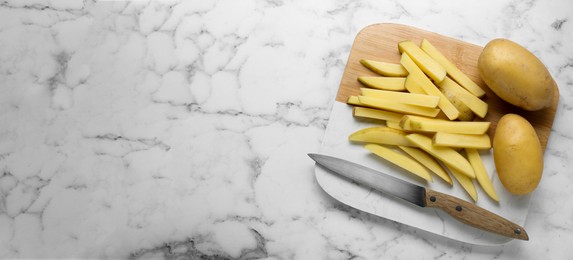 Photo of Whole and cut raw potatoes with knife on white marble table, top view. Space for text. Cooking delicious French fries