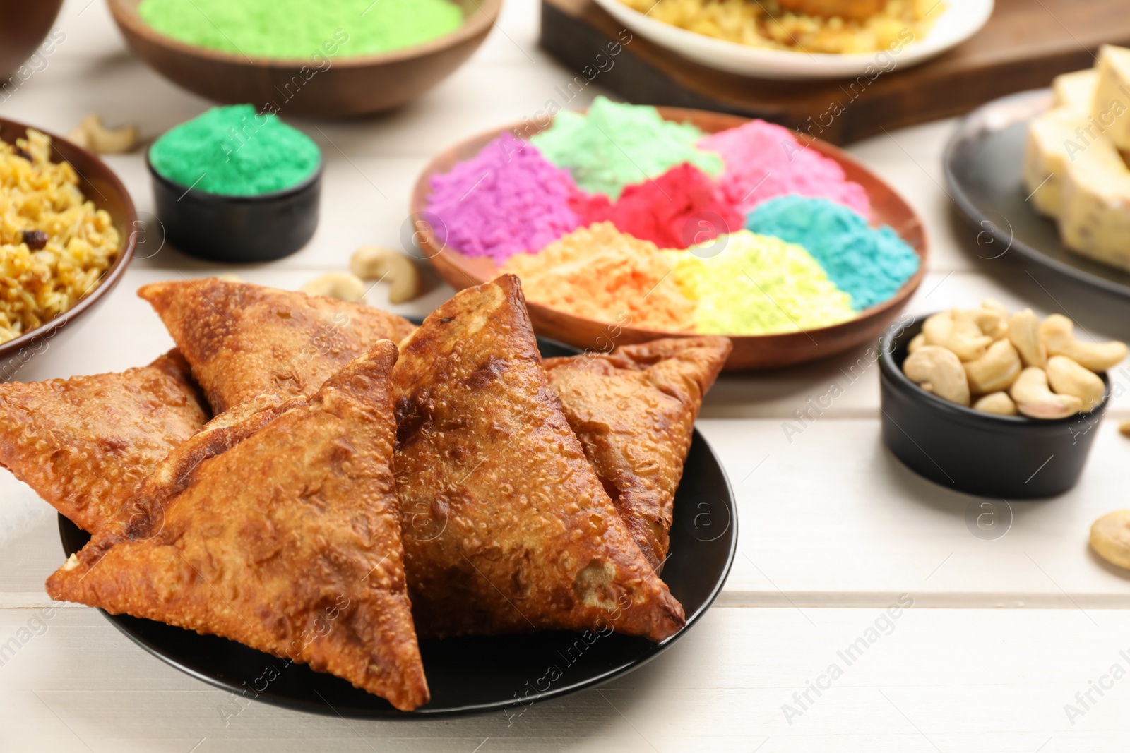 Photo of Traditional Indian food and color powders on white wooden table. Holi festival celebration