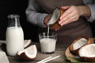 Photo of Woman pouring tasty coconut milk into glass at wooden table, closeup