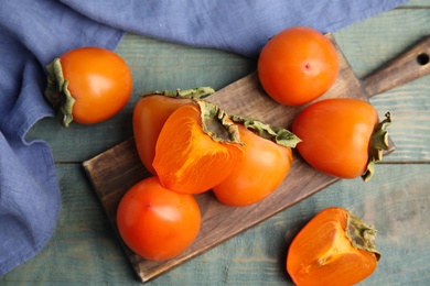 Photo of Tasty ripe persimmons on light blue wooden table, flat lay