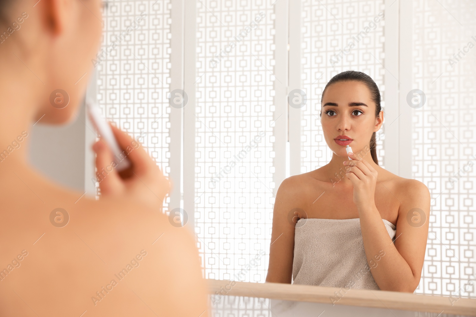 Photo of Woman with herpes applying cream on lips in front of mirror at home