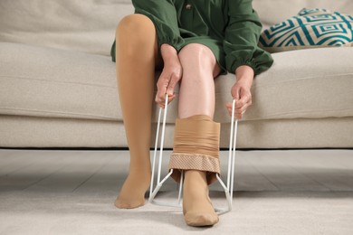 Photo of Woman putting on compression tights with stocking donner in living room, closeup. Prevention of varicose veins