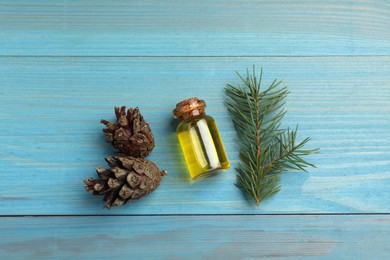 Photo of Pine essential oil, cones and branch on light blue wooden table, flat lay