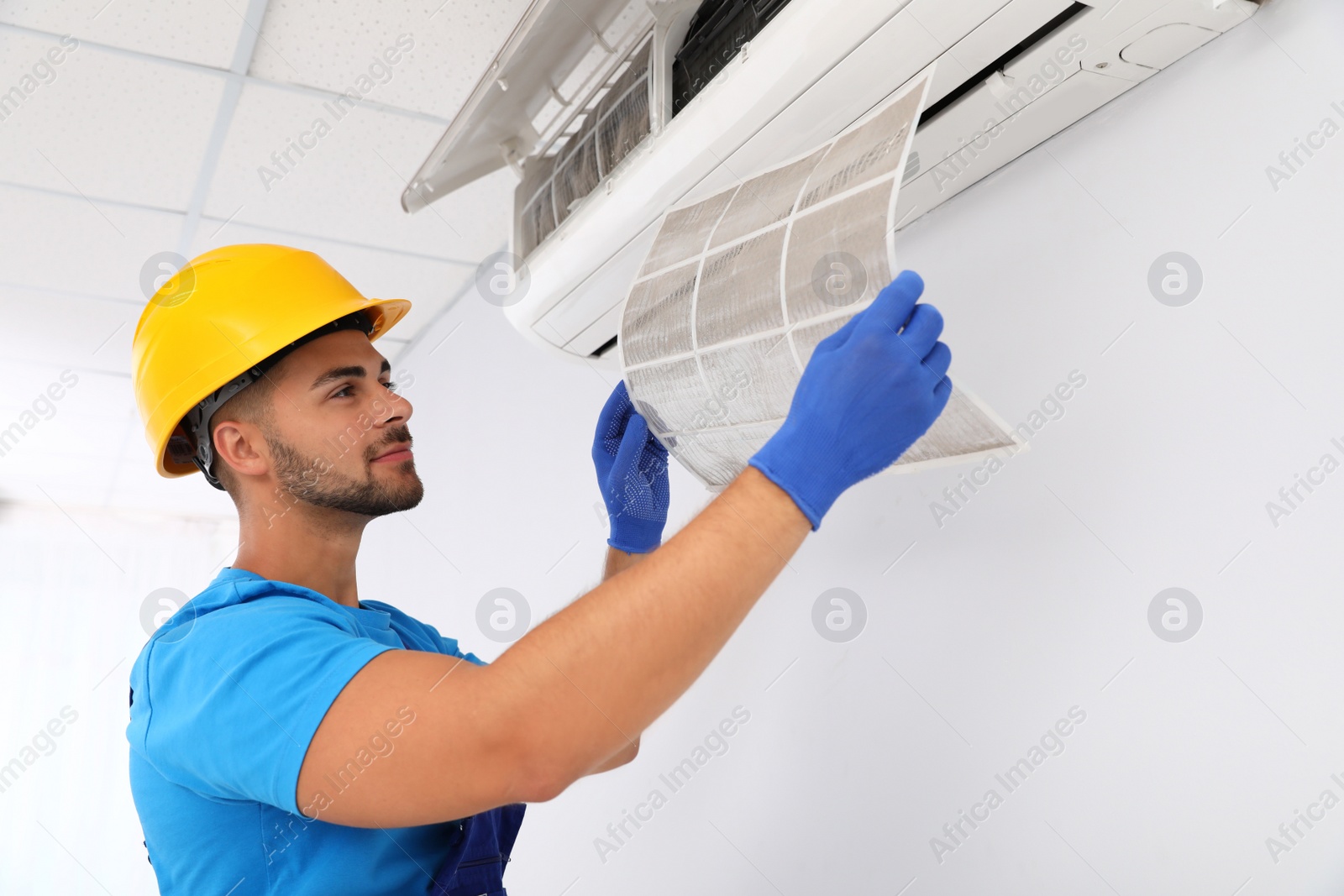 Photo of Professional technician maintaining modern air conditioner indoors