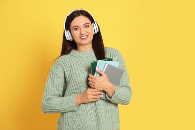 Young woman listening to audiobook on yellow background. Space for text