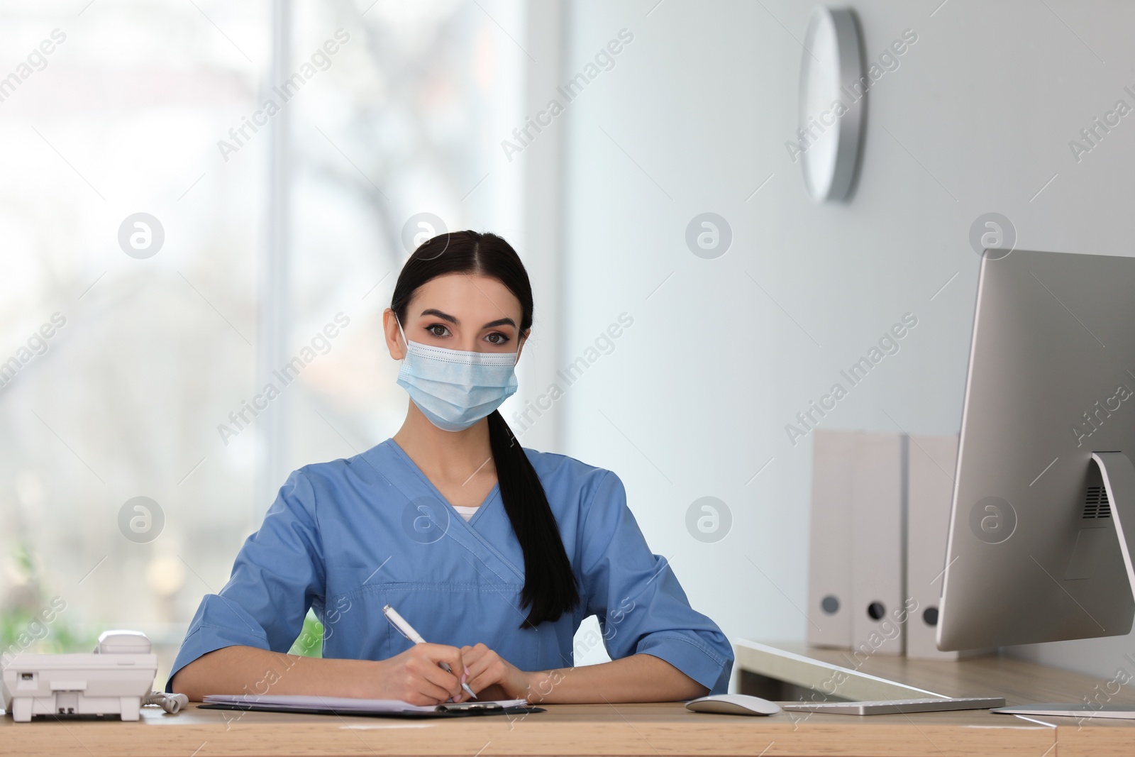 Photo of Receptionist with protective mask working at countertop in hospital