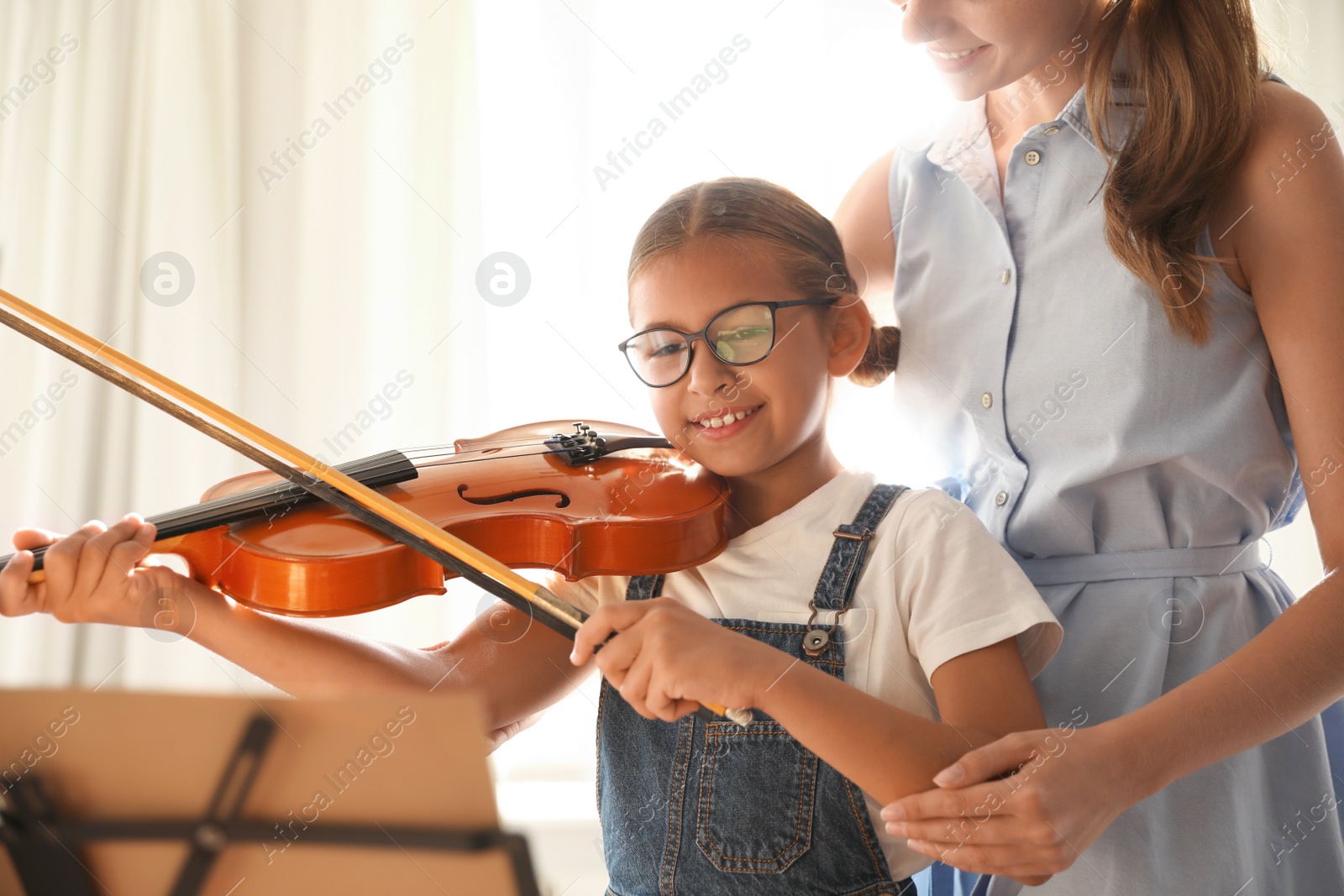 Photo of Young woman teaching little girl to play violin indoors