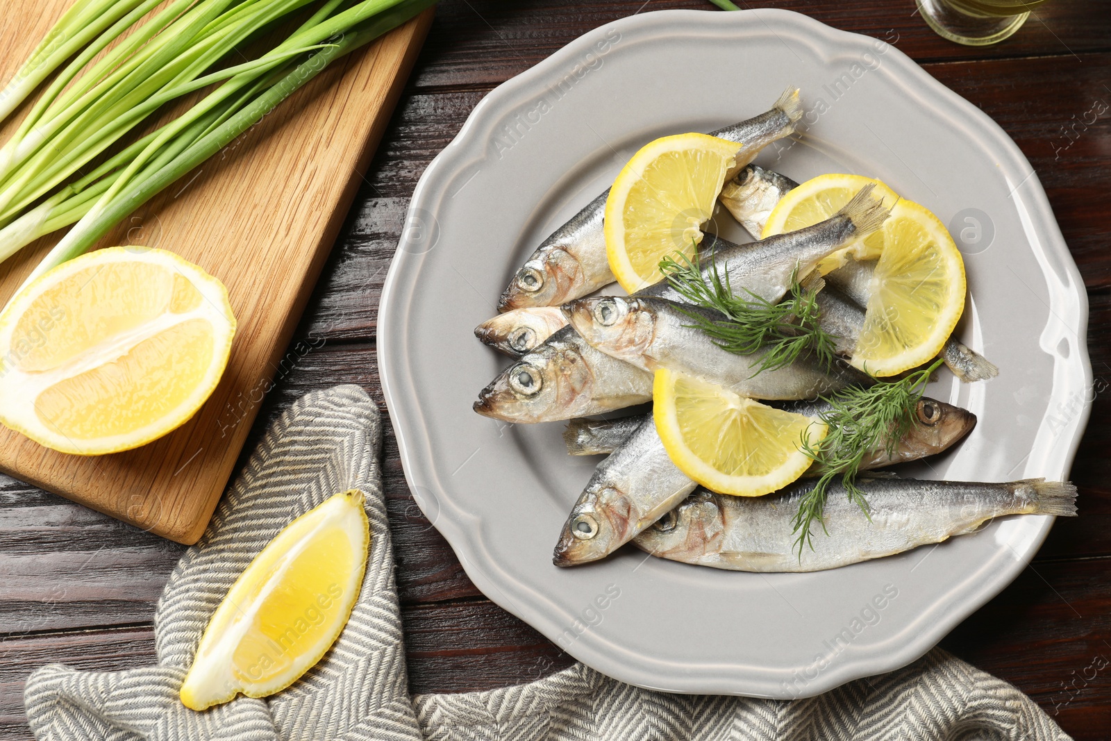 Photo of Fresh raw sprats, green onion, cut lemon and dill on wooden table, top view