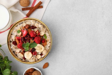 Photo of Delicious oatmeal with freeze dried berries, banana, nuts and mint on light grey table, flat lay. Space for text