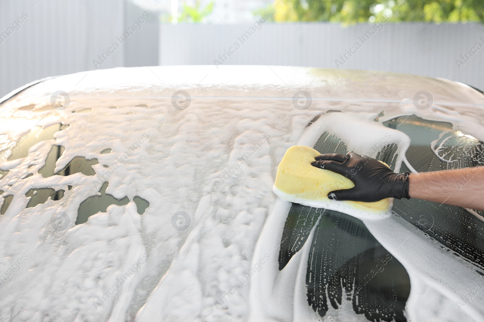 Photo of Worker cleaning automobile with sponge at car wash, closeup