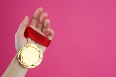 Photo of Woman holding golden medal on pink background, closeup. Space for design